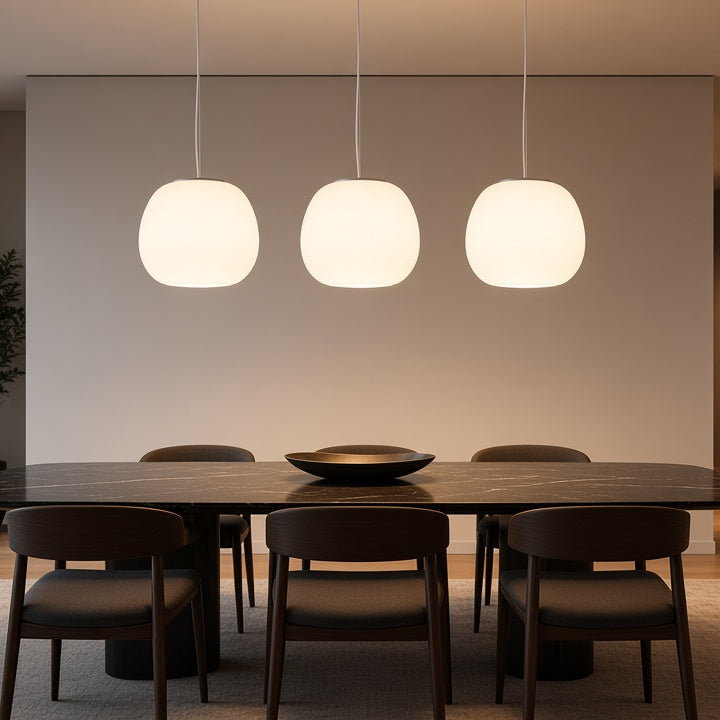 A modern dining room with a dark wood table and six matching chairs under three glowing spherical pendant lights. Large floor-to-ceiling windows on the left show a city skyline at dusk, and the room has warm wood flooring and a light rug.