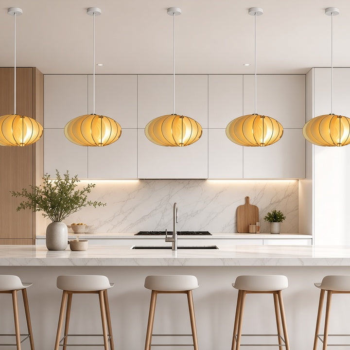 A modern kitchen interior with five ribbed pendant lights hanging over a white island and bar stools. The kitchen has white cabinets, a marble backsplash, and wood accents, with a large window on the right.
