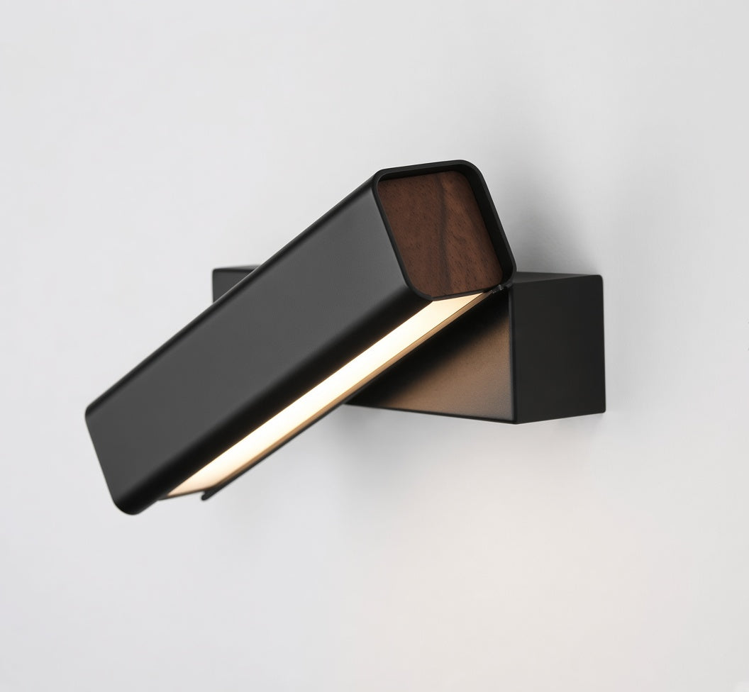 A modern wall-mounted light fixture with a matte black rectangular body, angled to illuminate a white wall, featuring a warm wood-grain accent panel on the top of the shade.