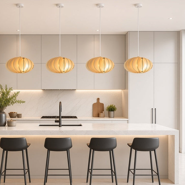A modern kitchen interior with a central island, five black bar stools, four hanging pendant lights, light wood cabinetry, and a large window looking out to greenery.